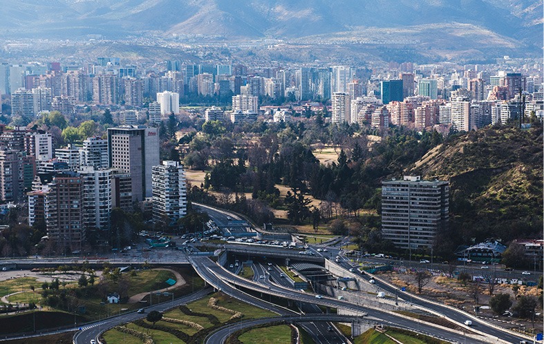 On the image, an aerial shot of the city of Santiago can 
                            be appreciated. There are highways connected and 
                            buildings. Also, there is a hill and, at the back, the Los 
                            Andes mountain range.